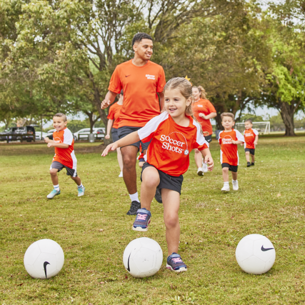 Soccer Shots coach and children running towards a row of soccer balls.