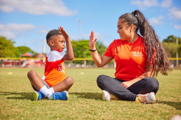 Soccer Shots coach and child sitting on Soccer Island giving a high-five