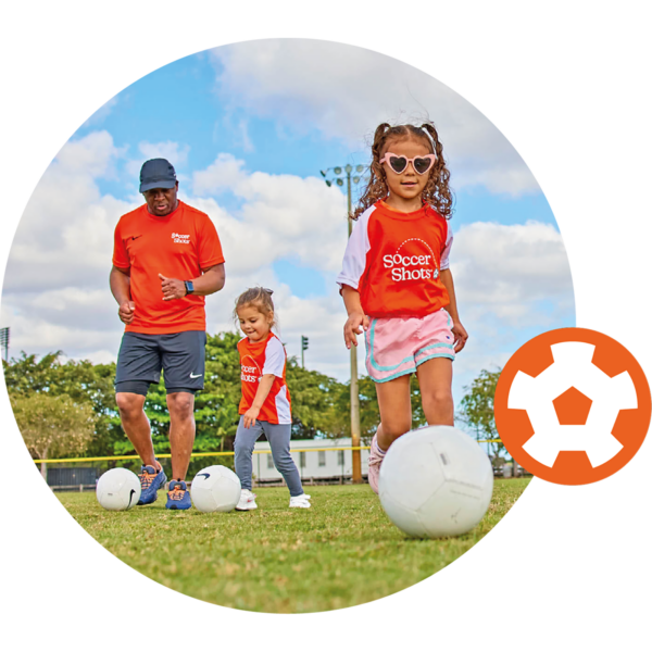 Girl dribbing soccer ball with sunglasses on. Coach and small child dribbling soccer ball in the background.